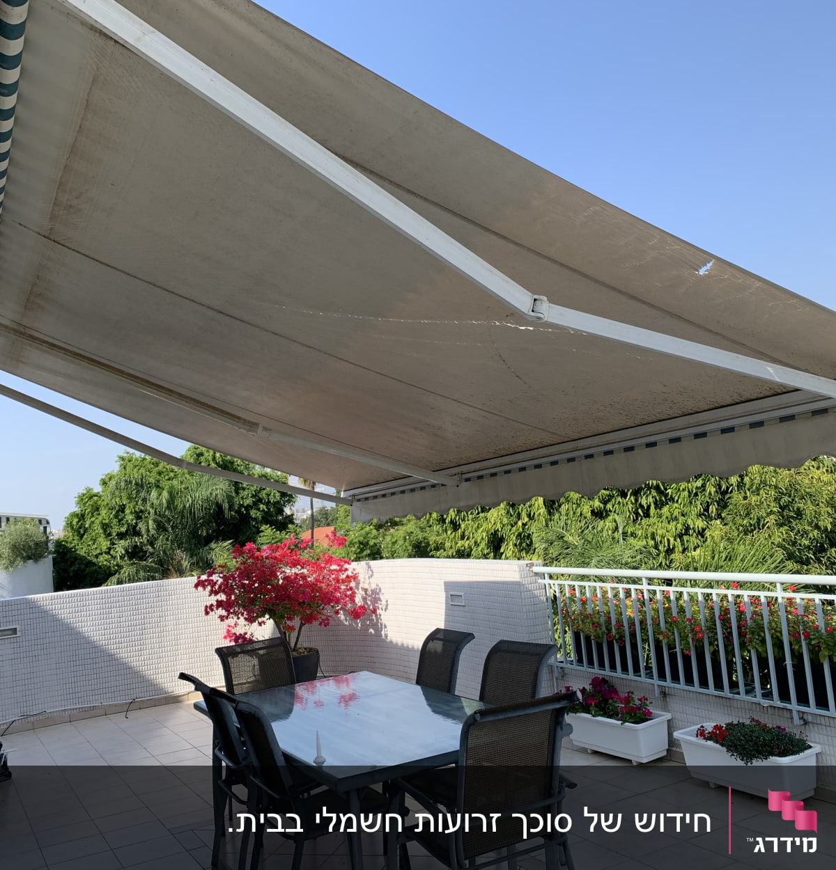 סוכך גדול נמתח מעל מרפסת עם שולחן וכיסאות.